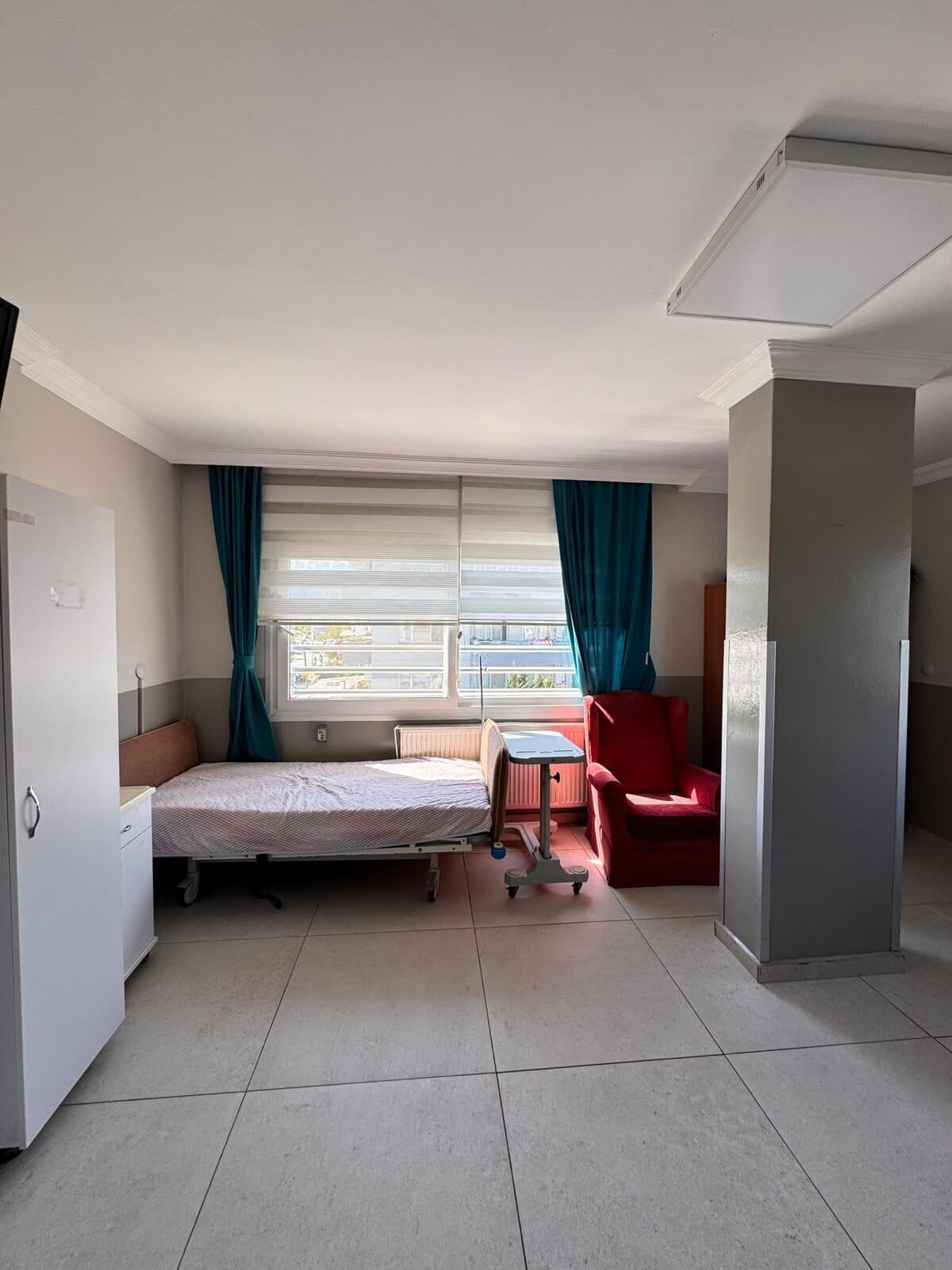 Pencereli bir sakin odası: hasta karyolası, refakatçi koltuğu ve dolap